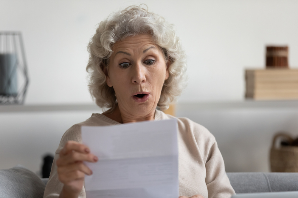 surprised middle aged mature woman looking at paper letter sitting alone on sofa