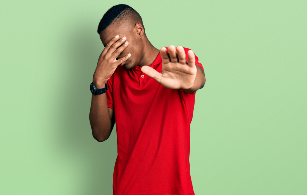 Young teenager wearing casual red t shirt covering eyes