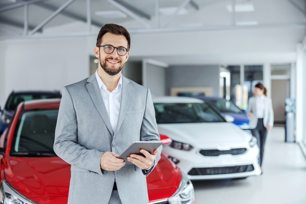 Smiling friendly car seller in car salon holding tablet