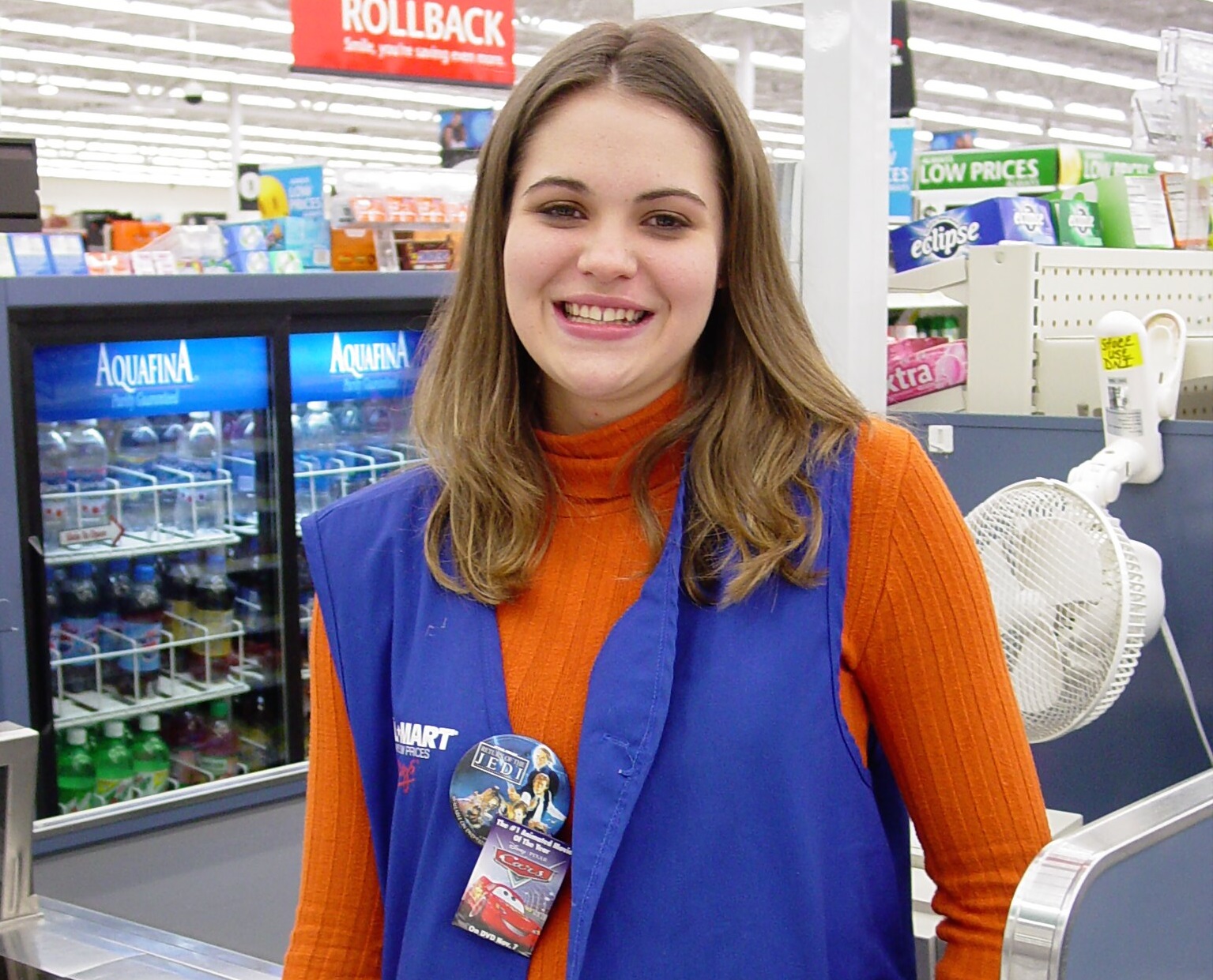 Woman wearing orange shirt and blue walmart jacket is smiling.