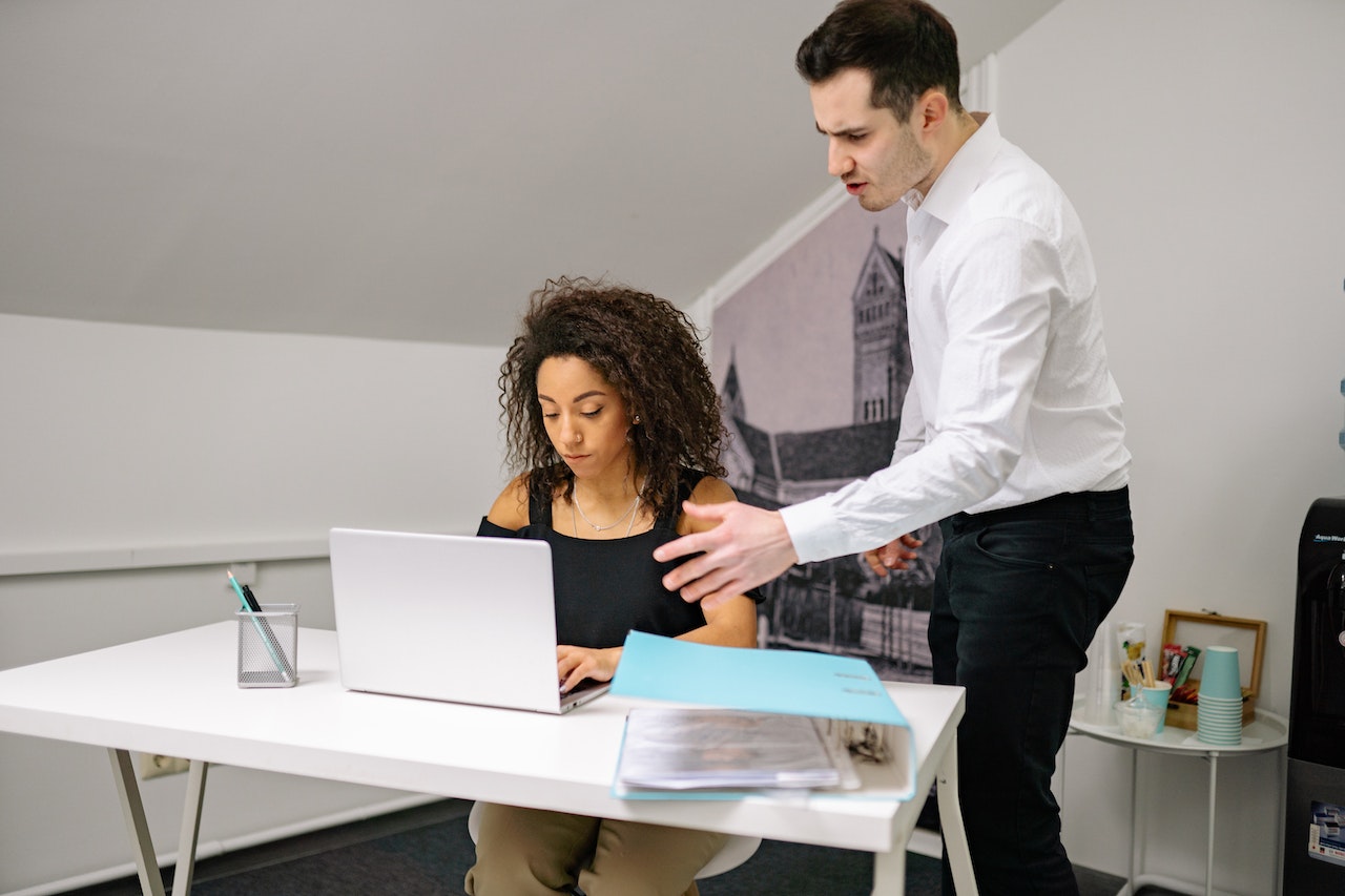 Young man is arguing with woman wearing black shirt and seating on her desk.