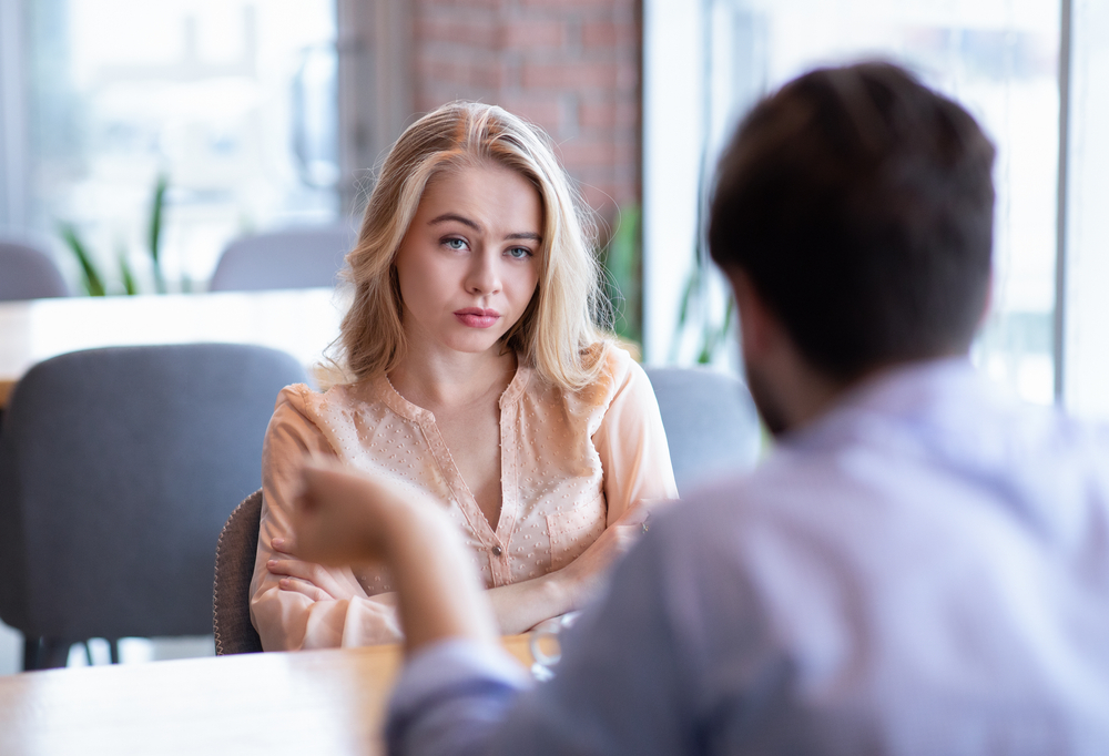Young woman feeling bored during dinner at café, unhappy with her boyfriend, disinterested in conversation