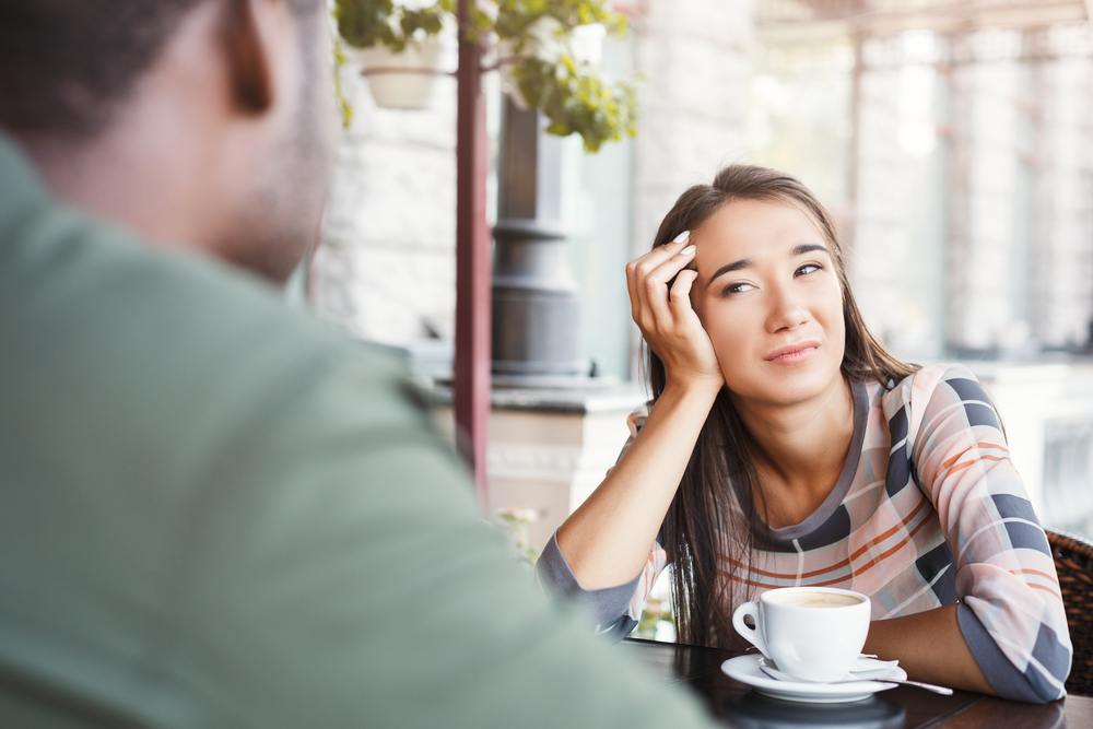 Young bored girl sitting and drinking coffee on date with her date at a café