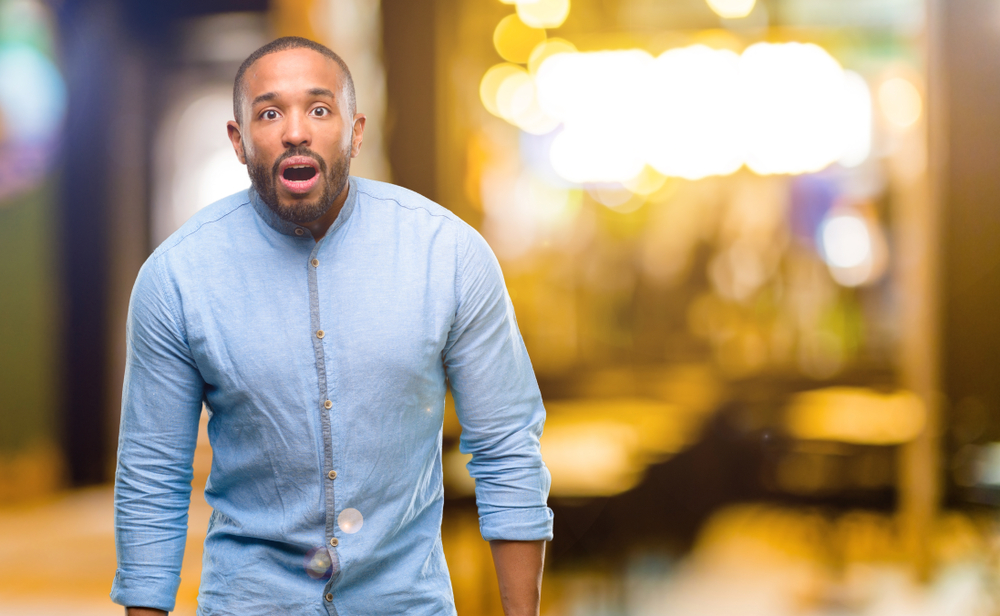 African American man with beard scared in shock, expressing panic and fear at night