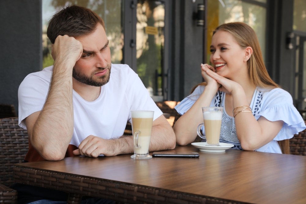 Young man having boring date with talkative girl in outdoor café