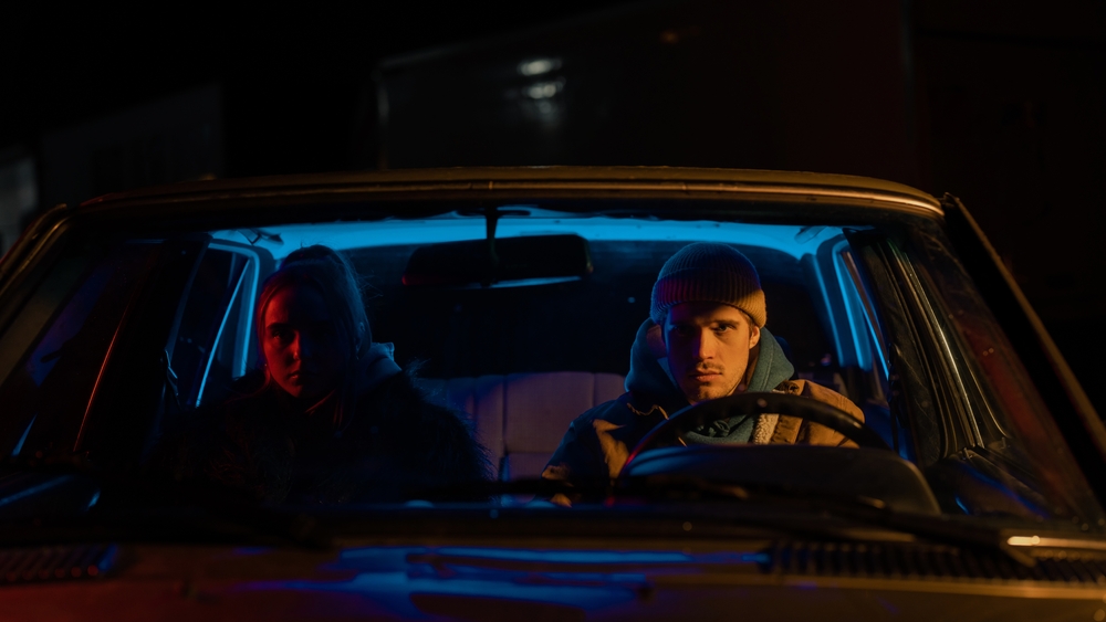 Beautiful Young Couple Sitting in Awkward Silence in a Vintage Looking Car with Neon Lights Surrounding Them