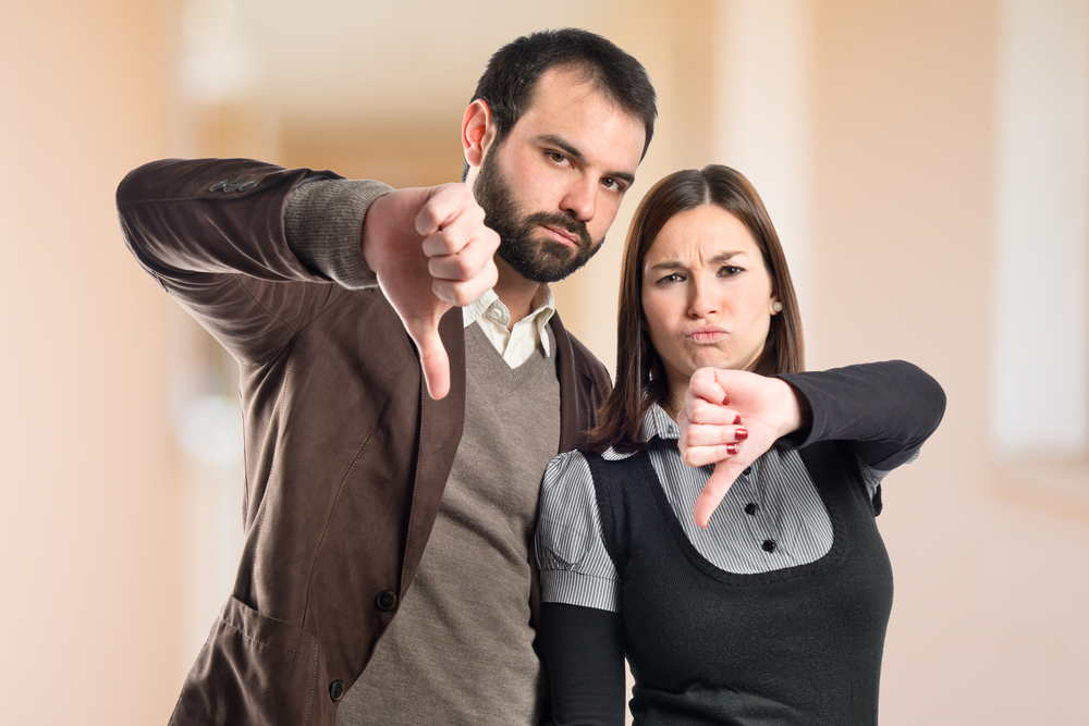 Unhappy couple showing thumbs down in front of blurred background