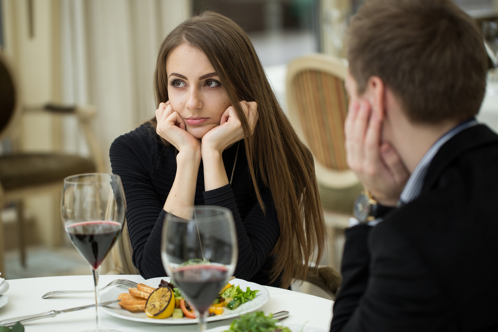 Young woman making an exasperated expression gesture on a bad date at the restaurant looking away from her date
