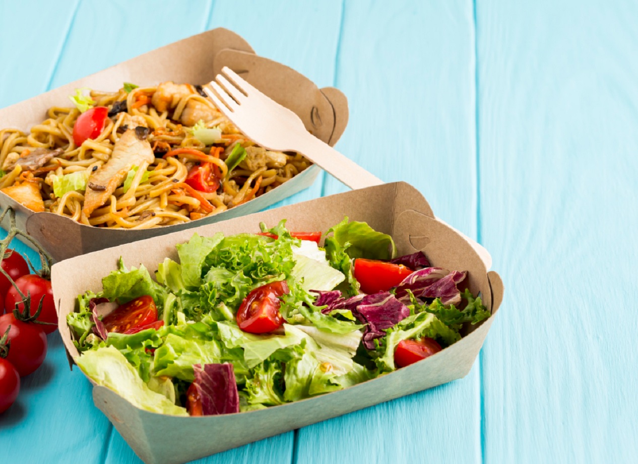 Food and salad in paper plates seating on the table.
