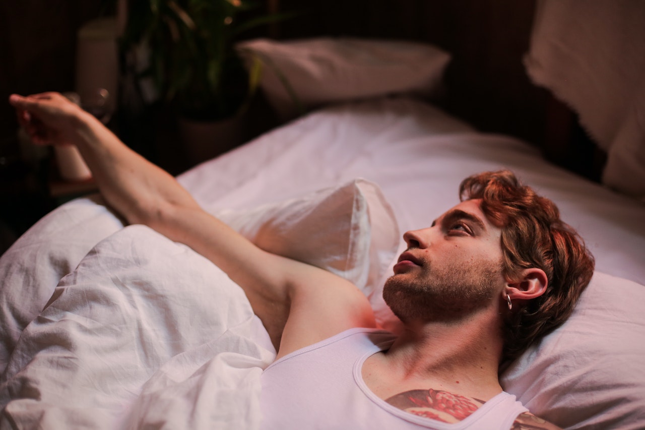 Young man wearing white shirt is laying on the bed.