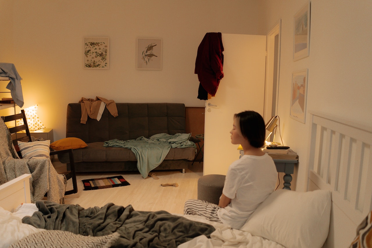 Young woman is seating on the bed inside a messy room.