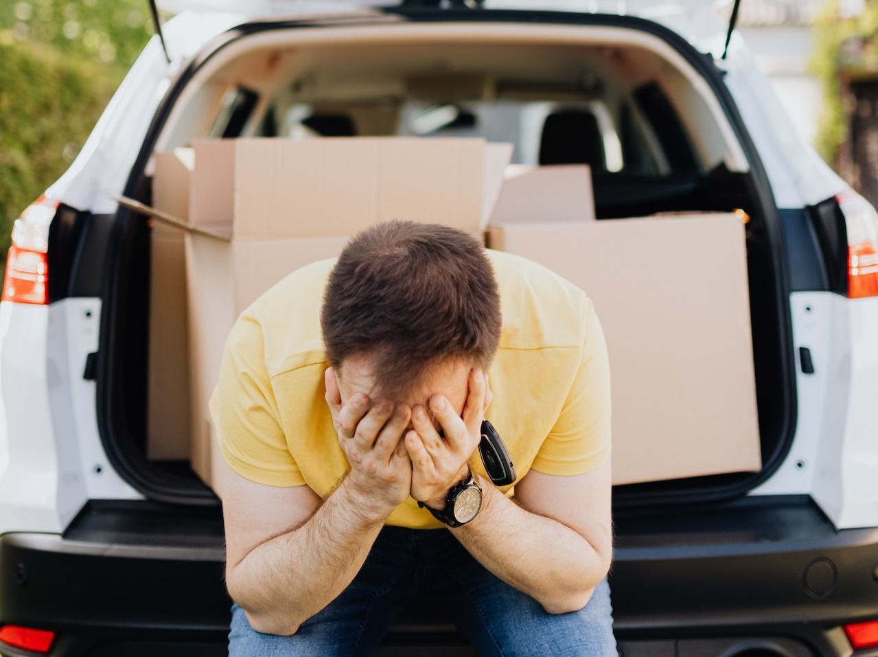 Worried man is seating in the back of the car full with boxes.