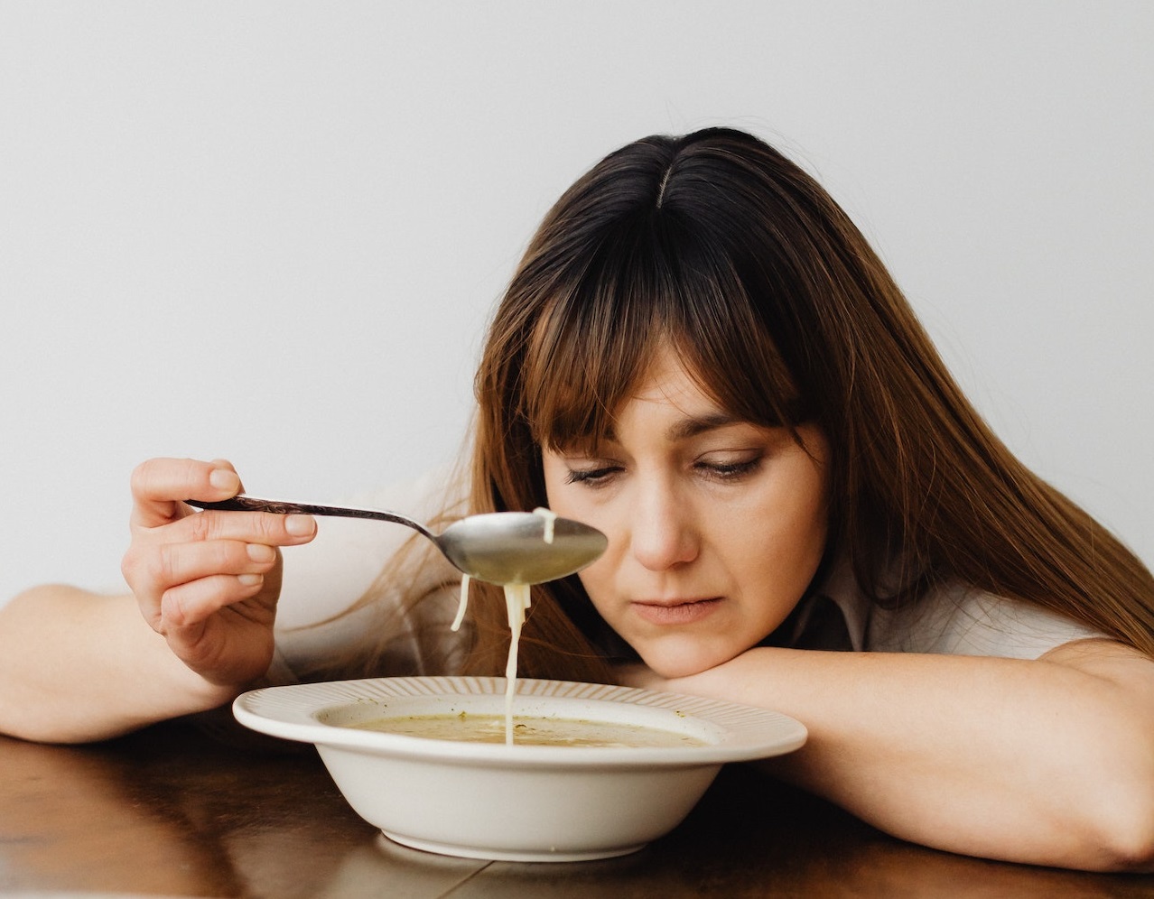 Sad woman is looking at plate full with soup.