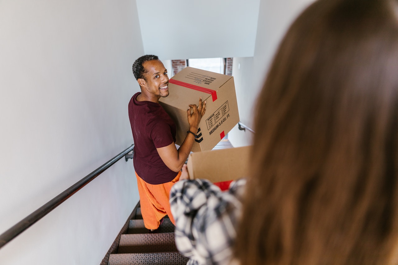 Man wearing red shirt is holding a box and walking down the stairs.