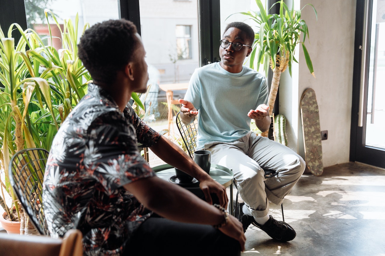Young male is talking to other young man seating in the chair.