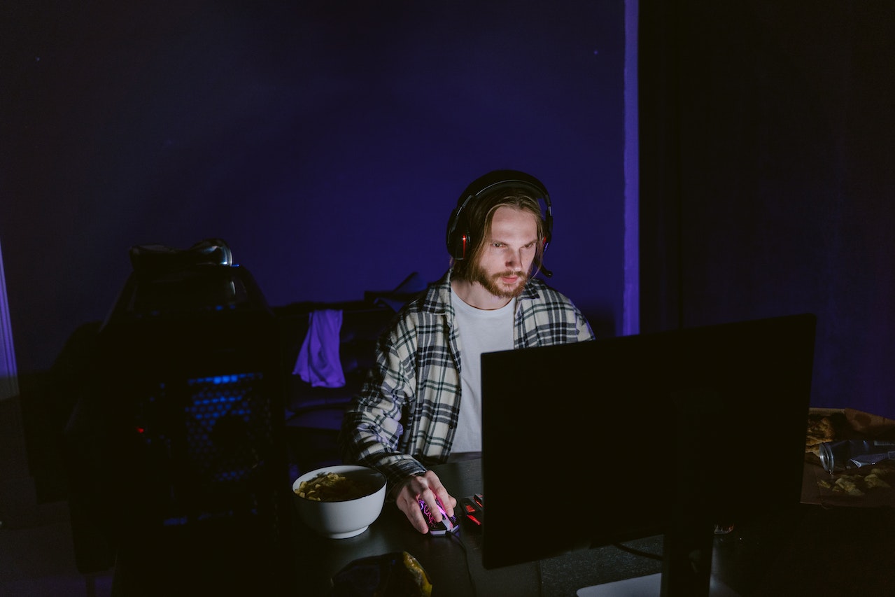 Man is playing a computer video game in dark room and eating.