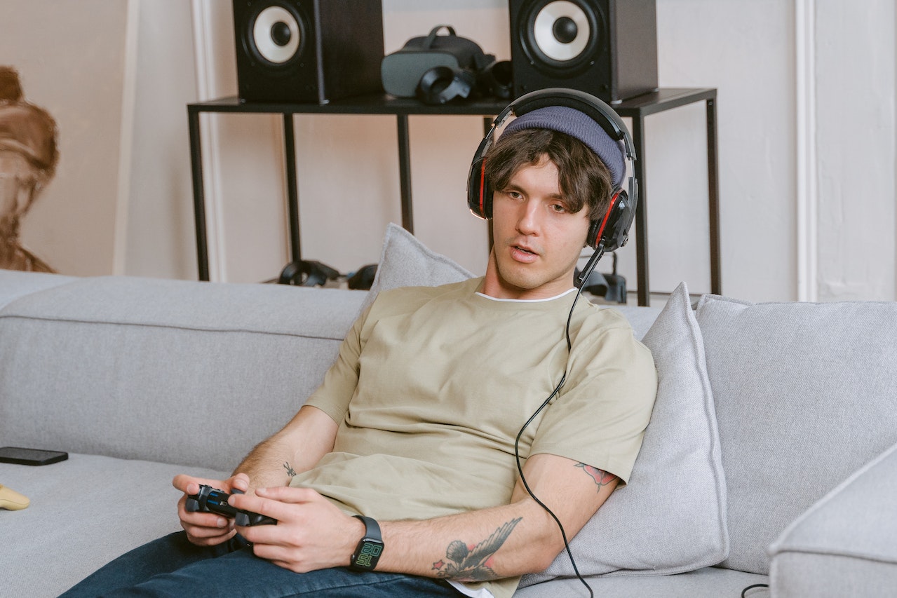 Young man wearing grey shirt is playing video games and seating on the sofa.