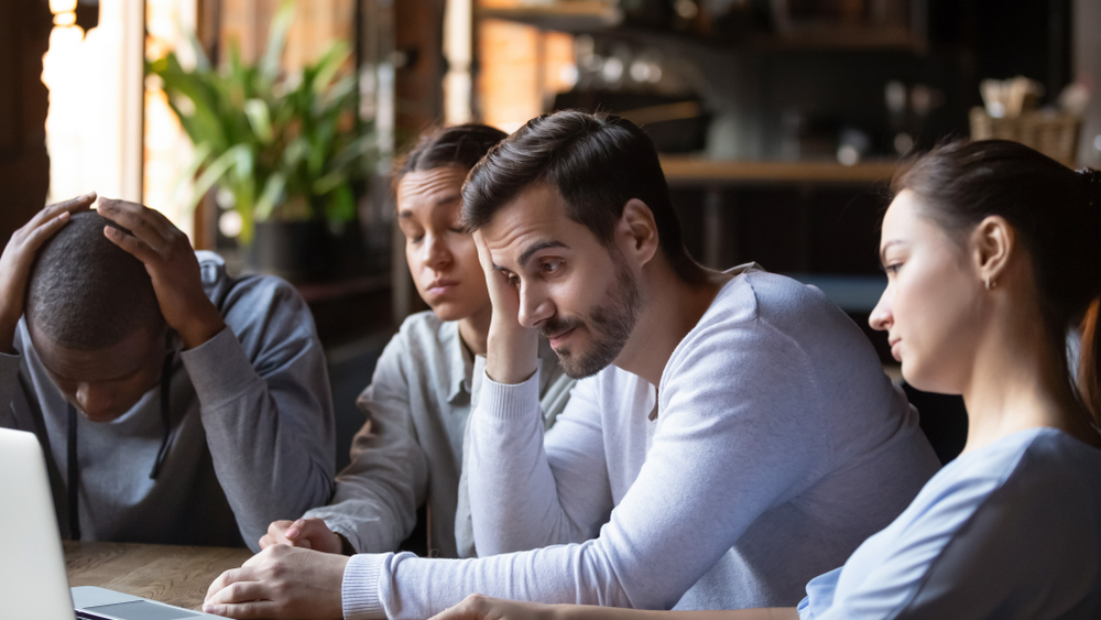 Disappointed multiracial millennial friends sitting at a café