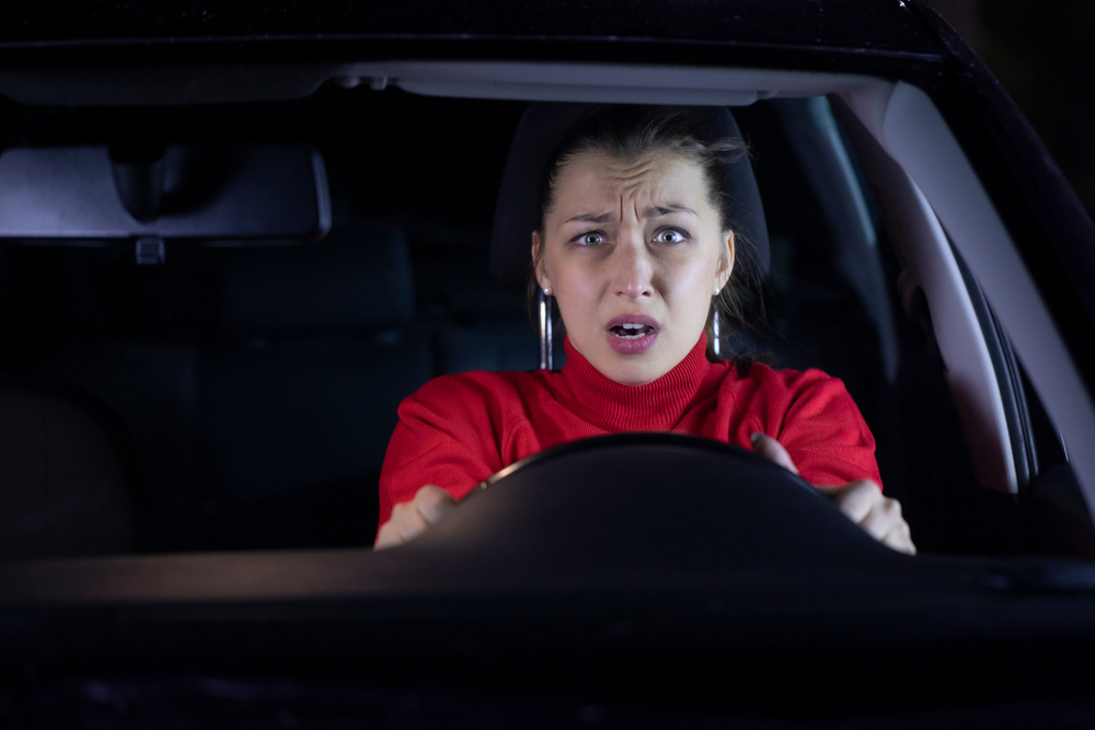 Shocked young woman in red top  driving a  car at night