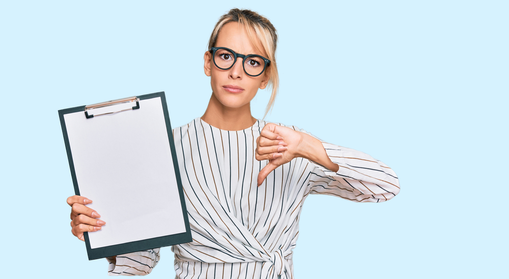 Beautiful blonde business woman holding clipboard with blank space with angry face