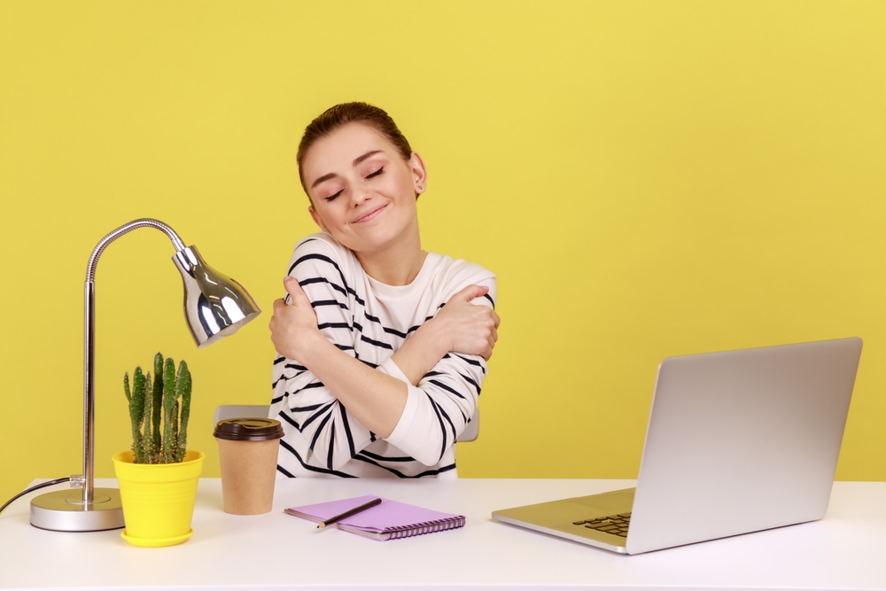 Selfish happy woman office manager embracing herself , sitting at workplace, feeling proud and satisfied