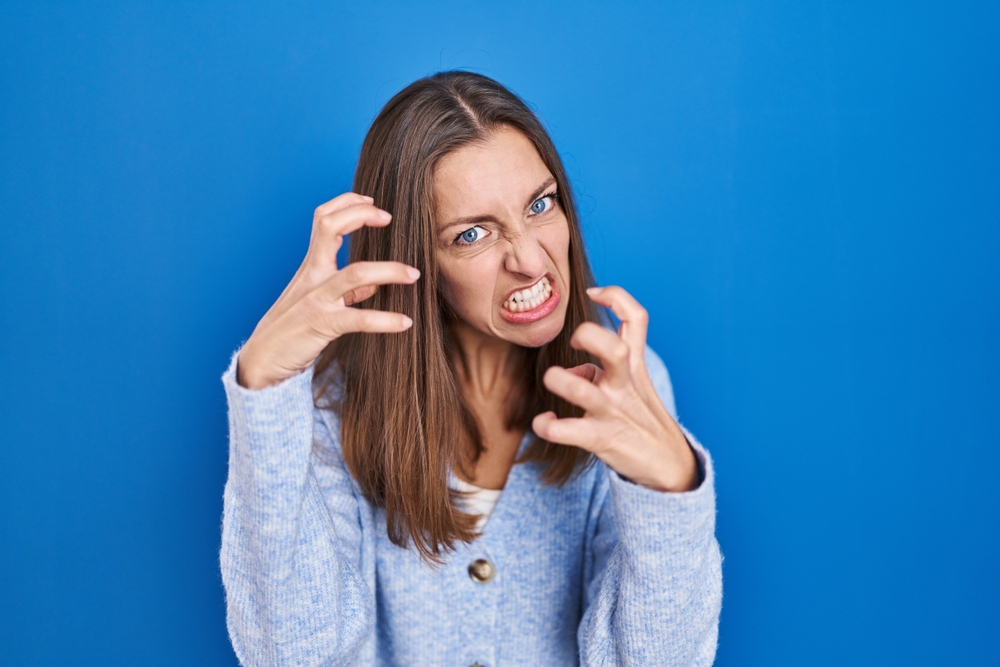 Angry woman  shouting frustrated with rage standing over blue background looking at the camera