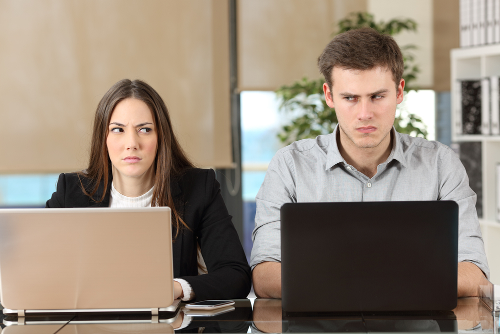 Front view of two angry business people using computers disputing at workplace