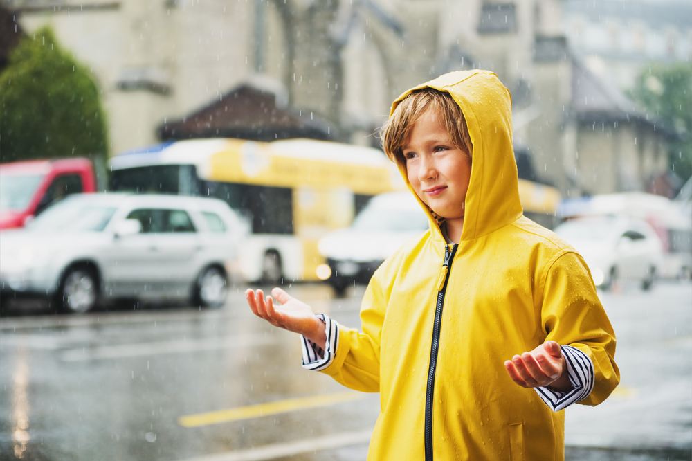 Cute little boy playing under the rain in a city