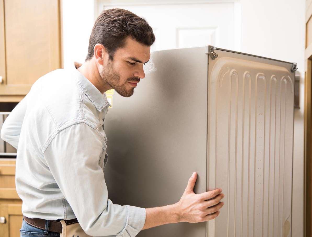 Young man is moving out the fridge from the kitchen.