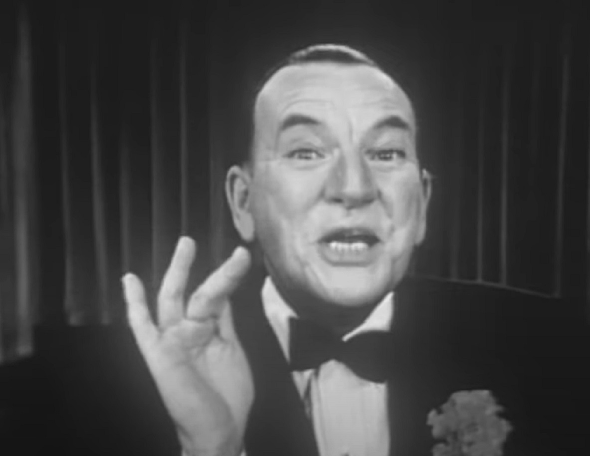 B&W Screenshot: Noel Coward is looking at camera, smiling and making  hand gesture - from Mad About the Boy: The Noel Coward Story (2023)