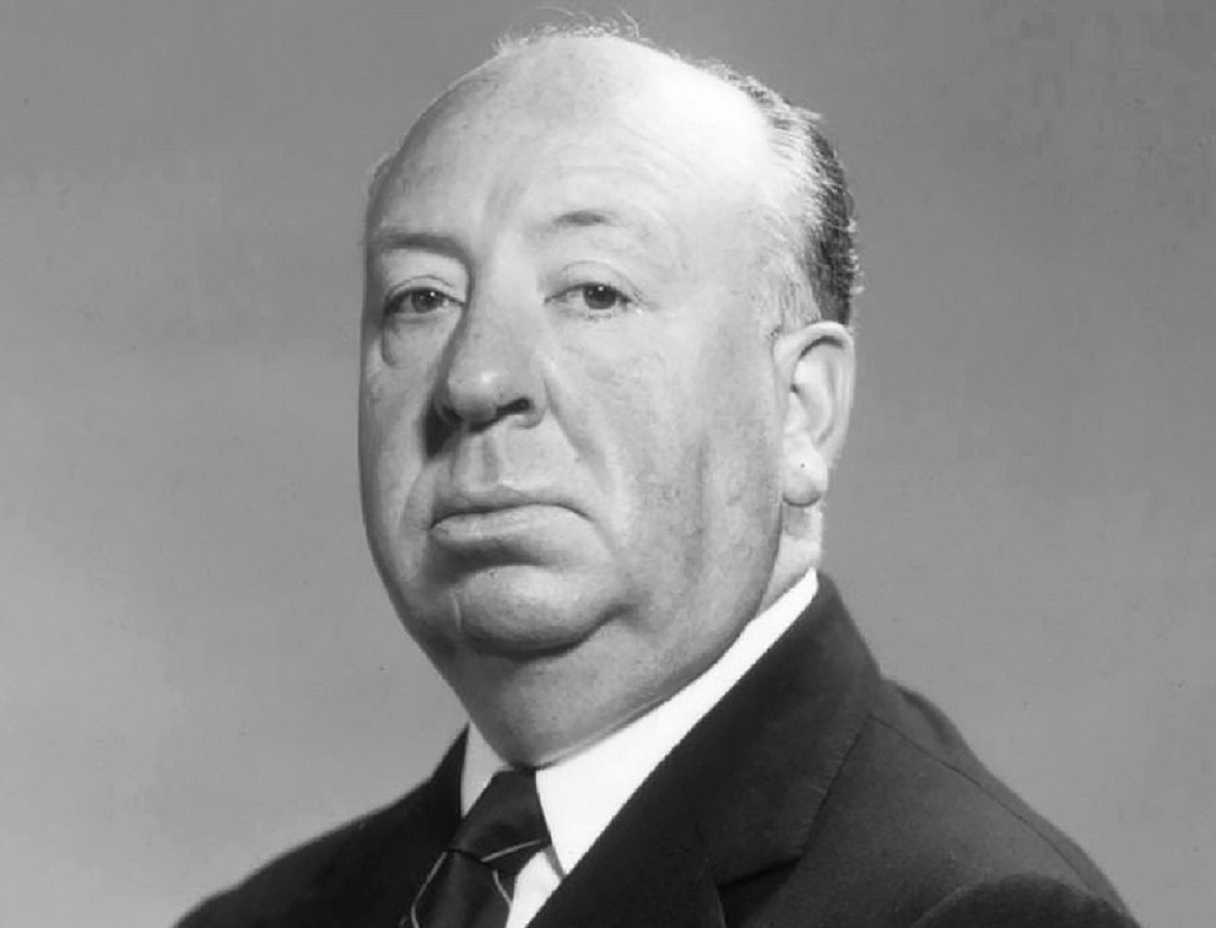 B&W photo of Alfred Hitchcock wearing black suit and looking at camera - 1955