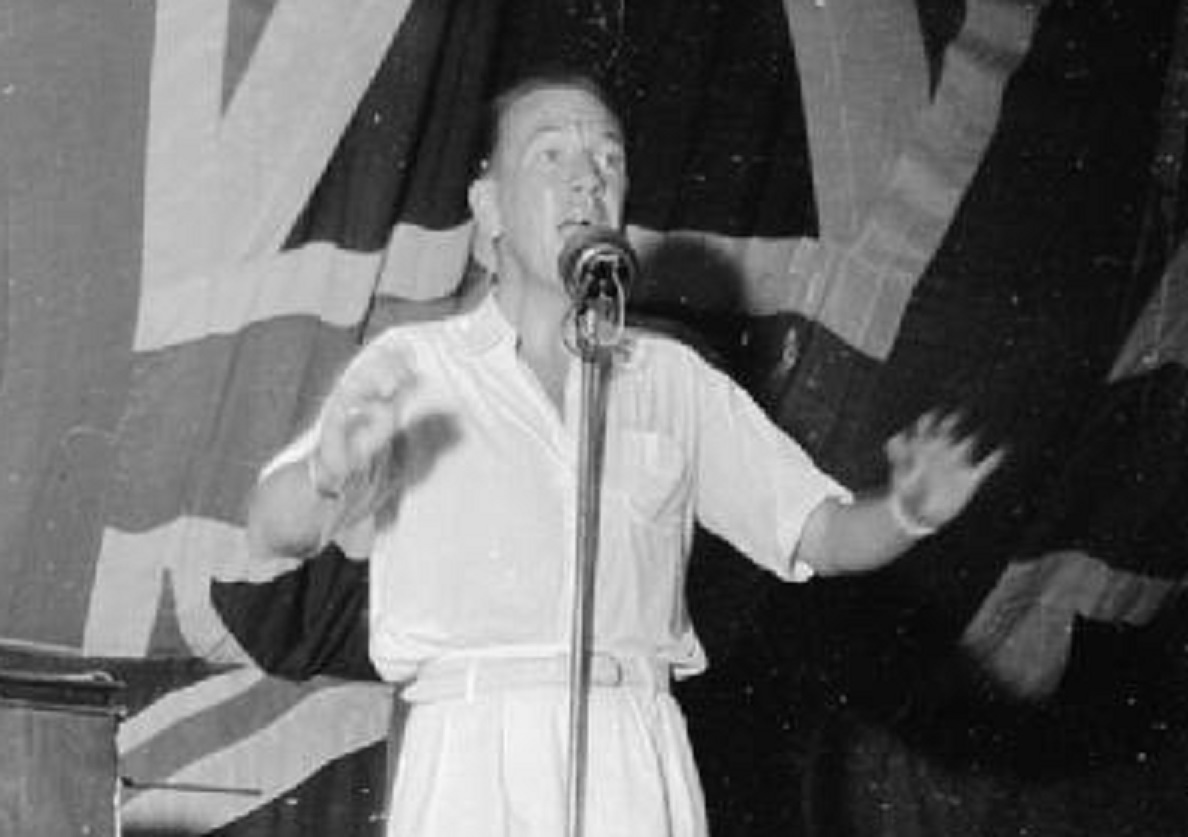 B&W photo of Noel Coward entertains people looking at front and singing - 1944