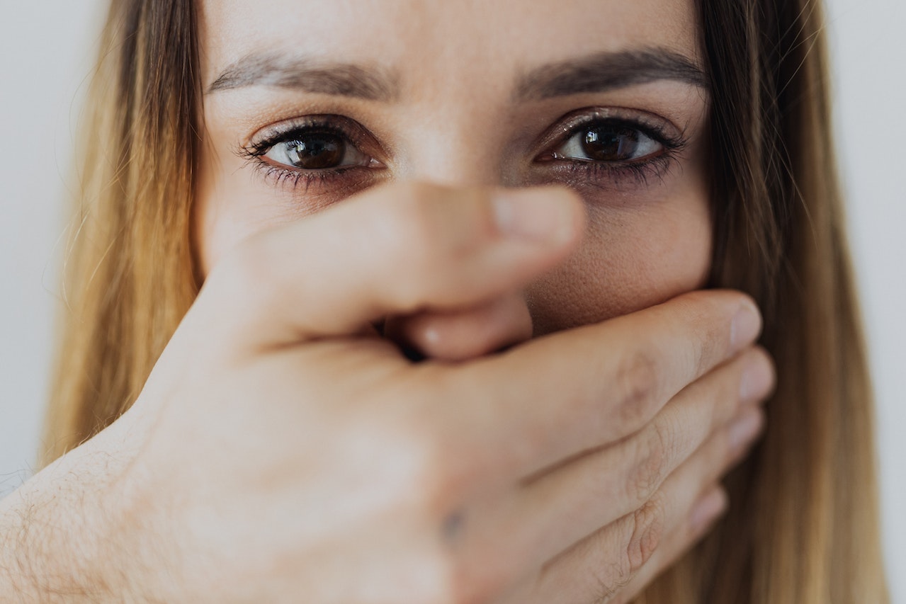Scared woman looking at front with hand covering her mouth.