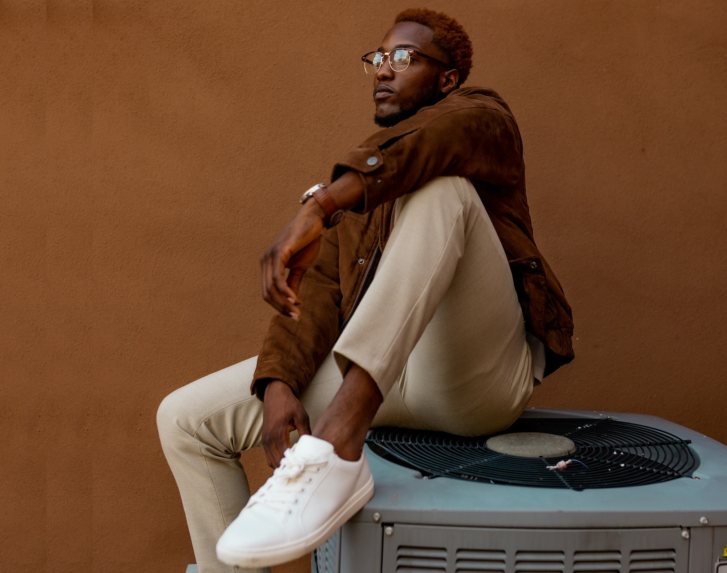 Black man is on top of air conditioning unit outside.