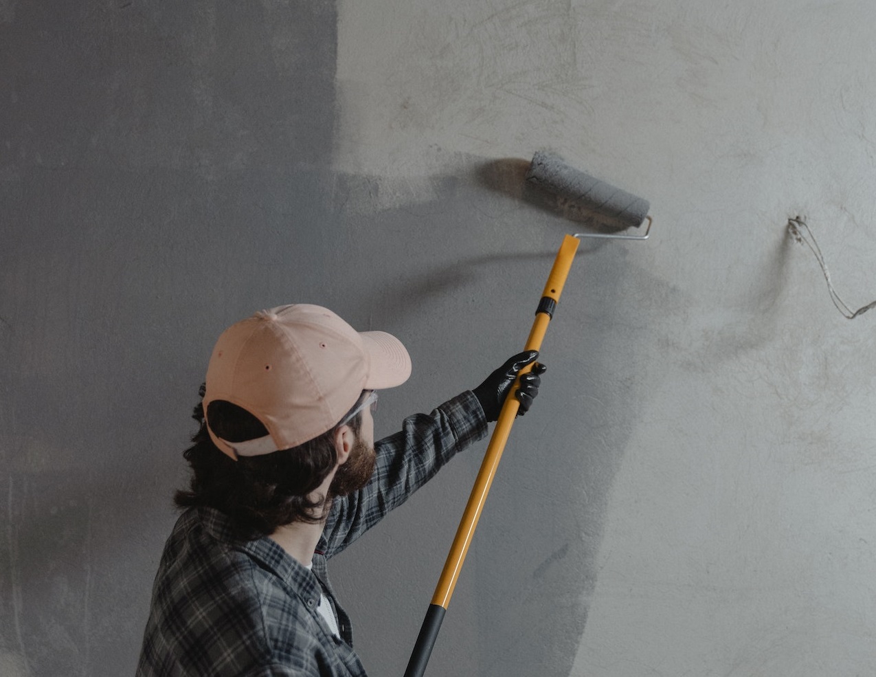 Man wearing grey shirt and hat is painting a wall in the office.