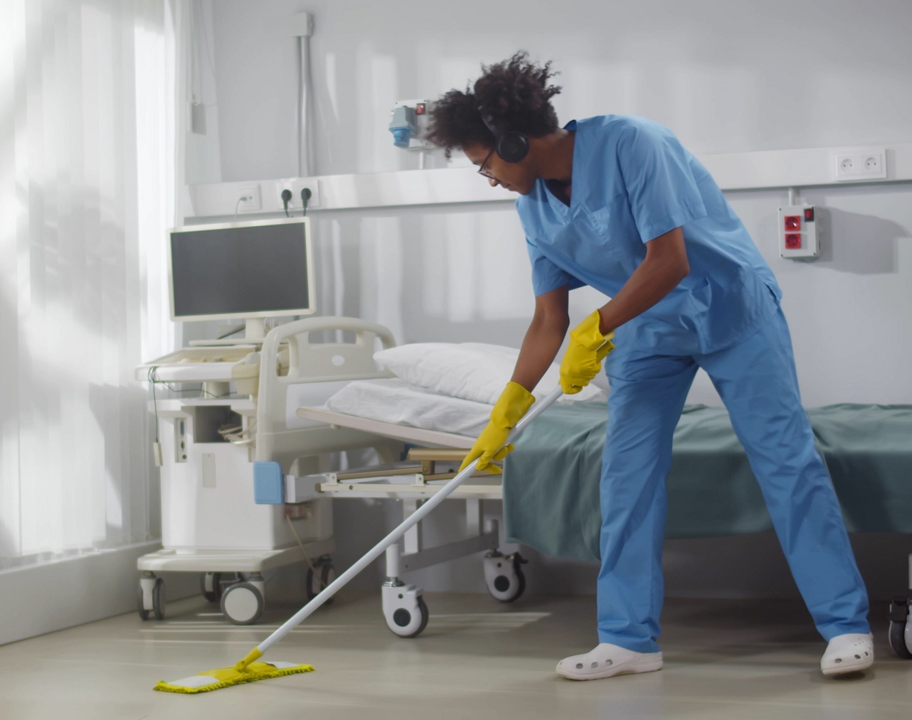 Young african man nurse is cleaning floor with mop in clinic room.