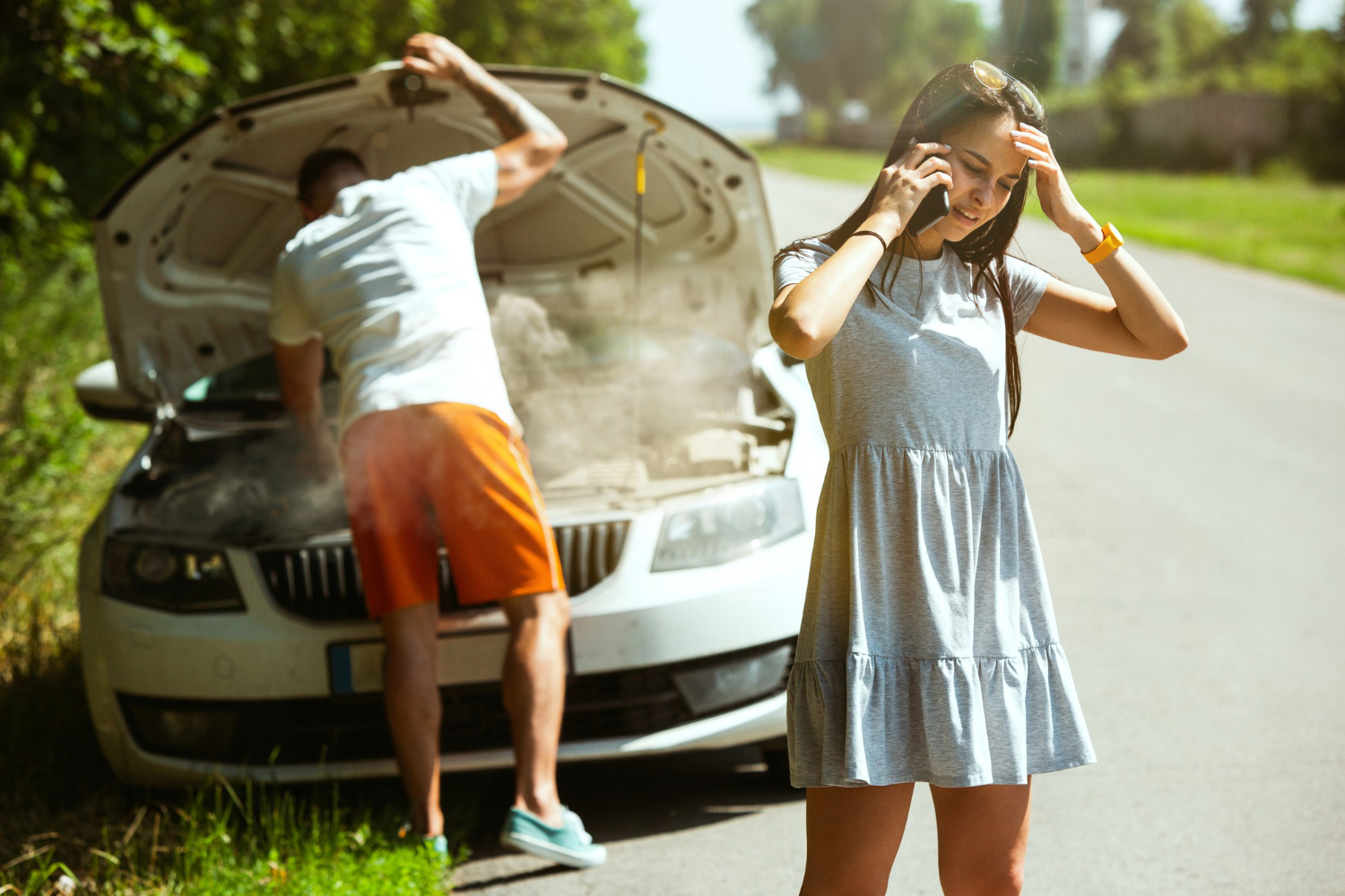 Man looking inside an car engine on damaged car while young woman are talking on the phone.