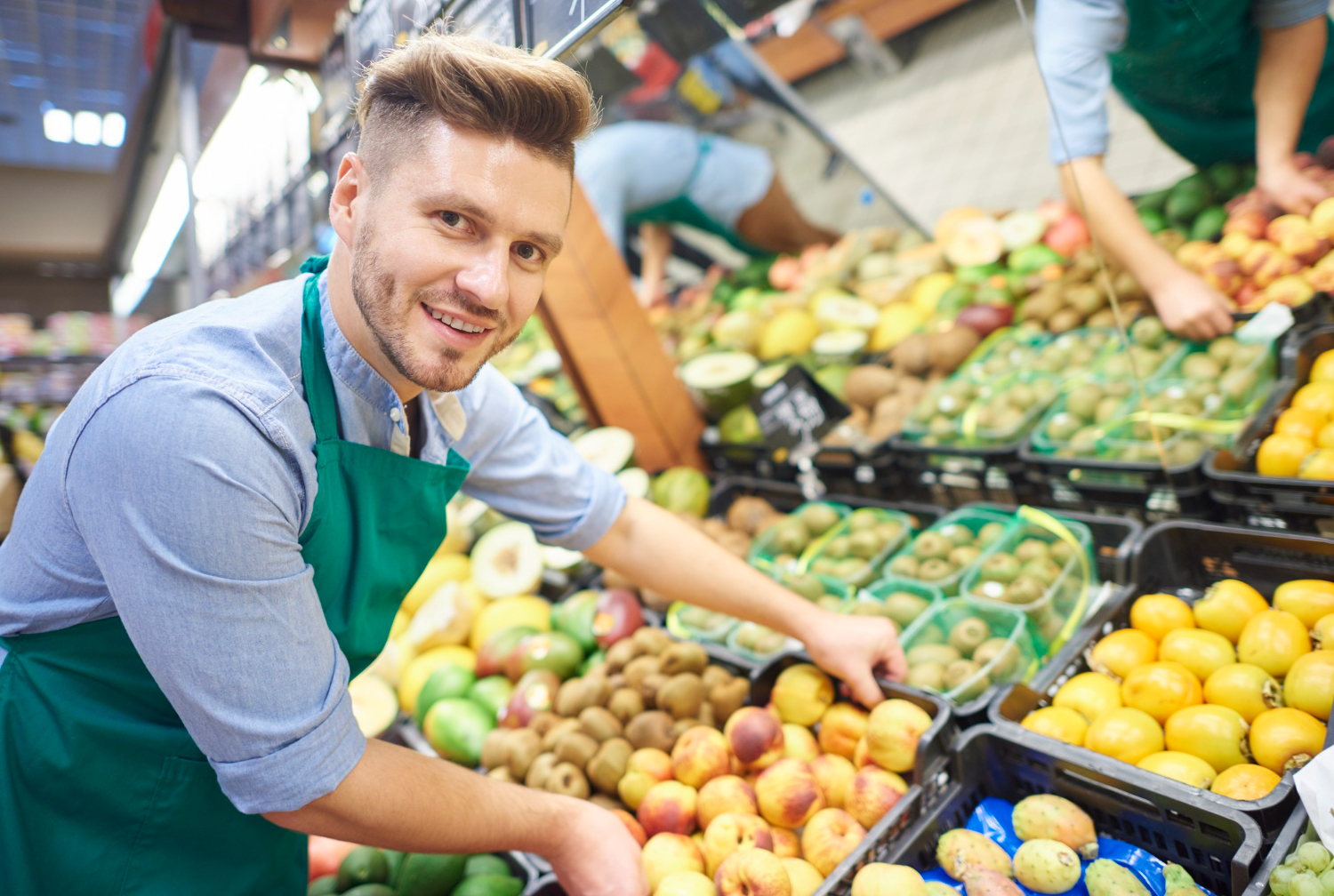 Young man wearing blue shirt is smiling while working on supermarket.