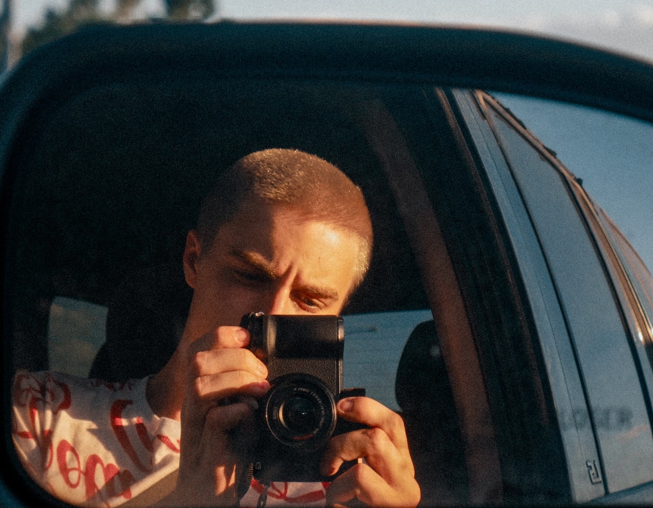 Young man is taking photos with digital camera from his car.