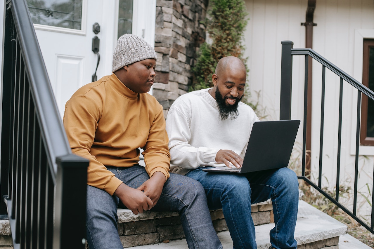 Black businessman is browsing on laptop with his son.