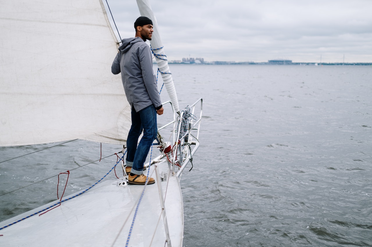 Man wearing grey jacket and hat is standing on a boat.