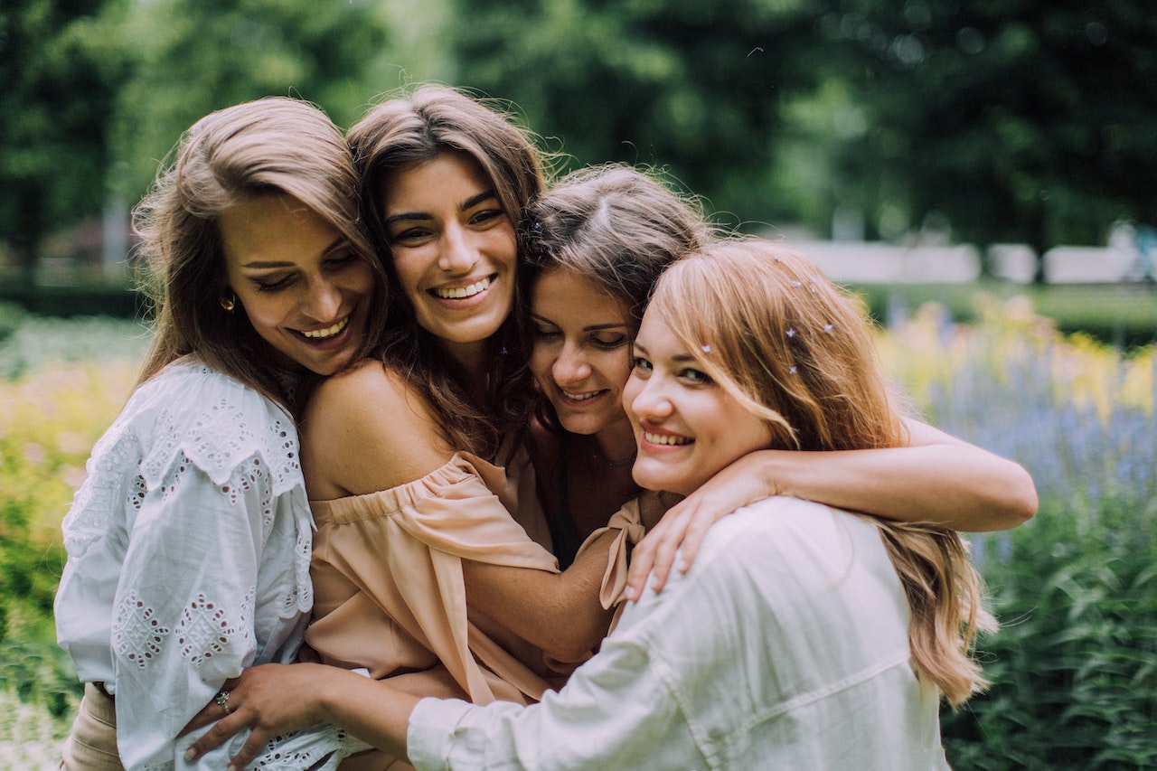 Four girls are hugging and smiling outside.