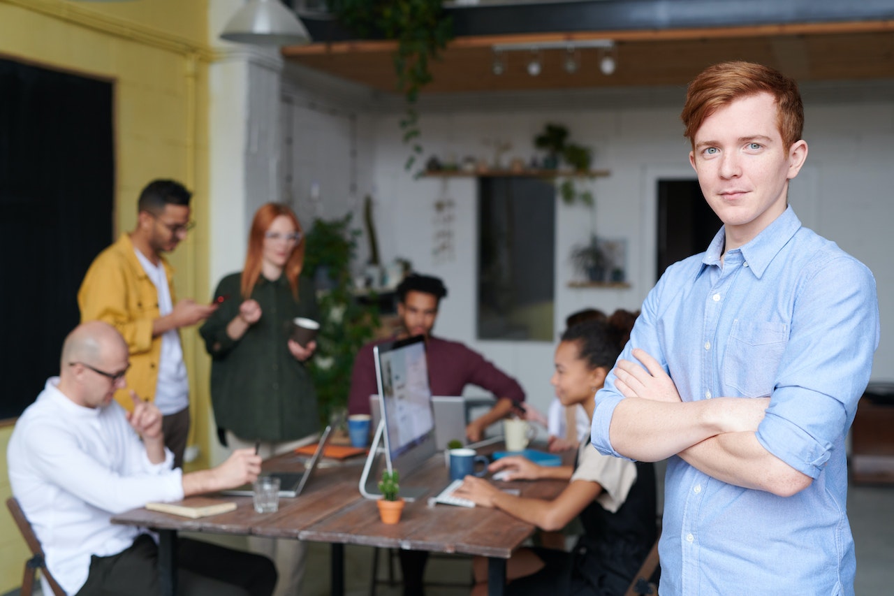 Man is standing beside other people who are sitting on the table with laptops.