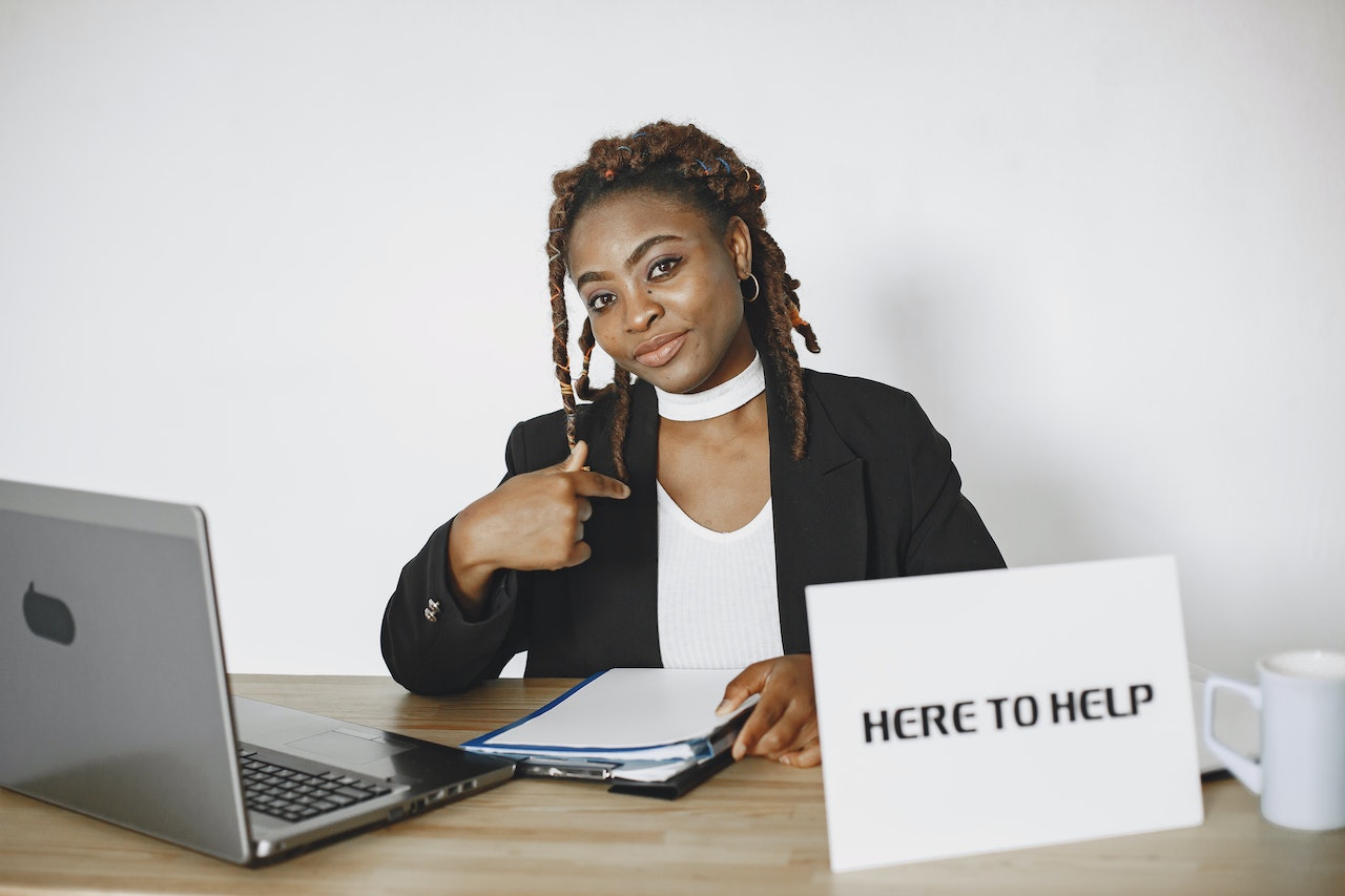 Young woman is seating on her desk and smiling with sign
