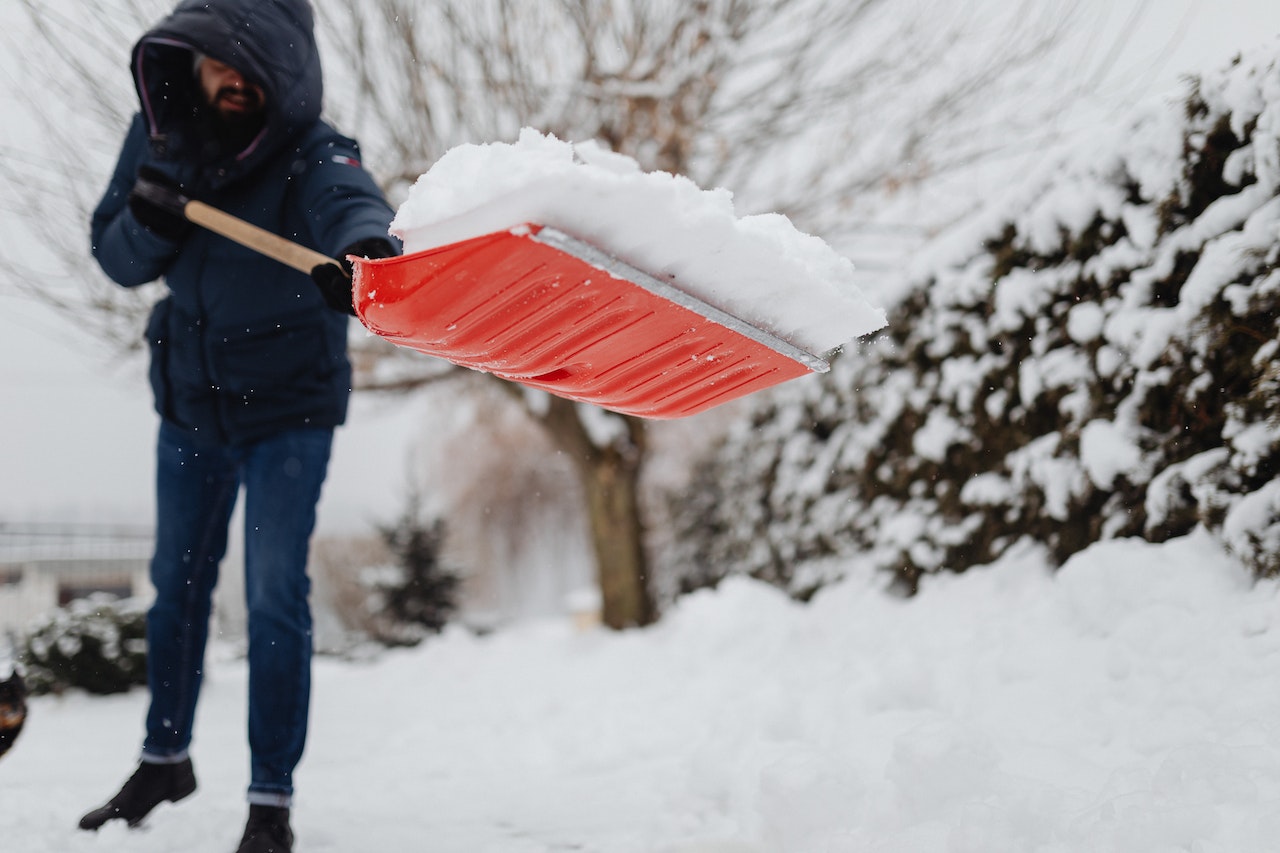 Man is shoveling the snow with red shovel outside.