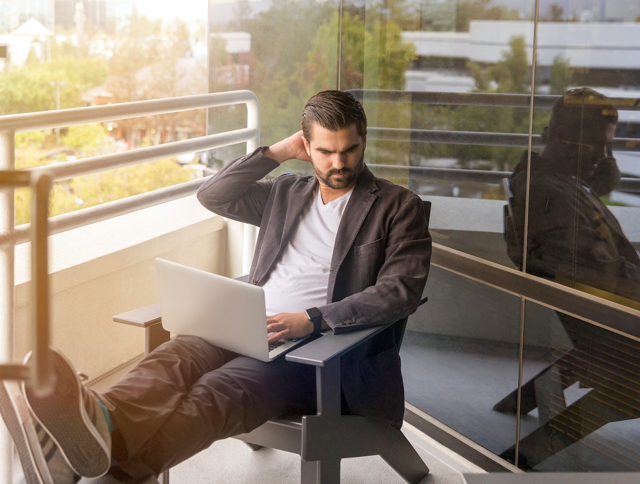 Man is seating on the balcony and working on laptop.