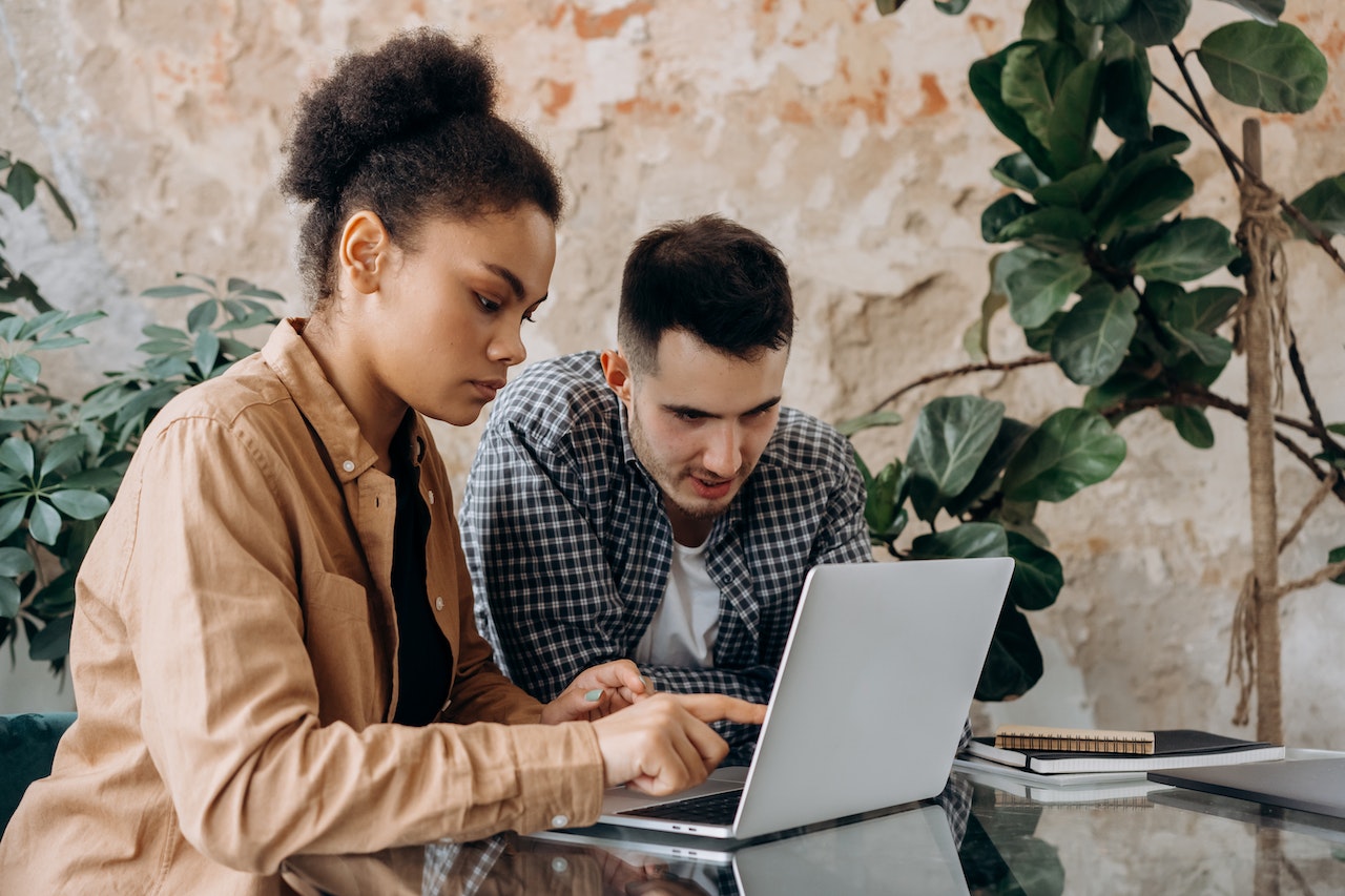 Two people are seating on the desk and looking at laptop.