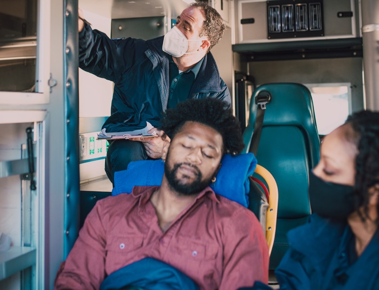 Black man wearing red shirt is seating in the back in the ambulance.