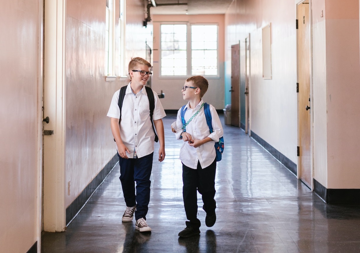 Two young kids are talking and smiling at school hallway.