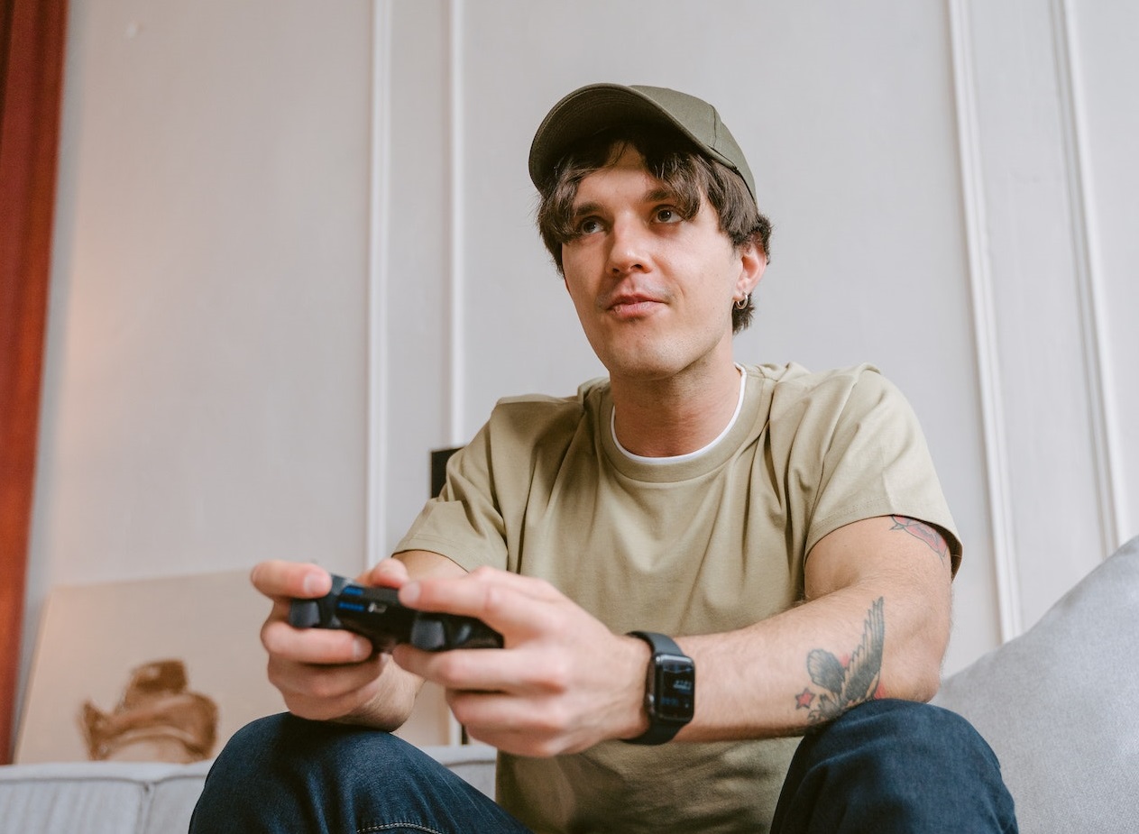 Man wearing grey shirt and hat is playing video game on the sofa.